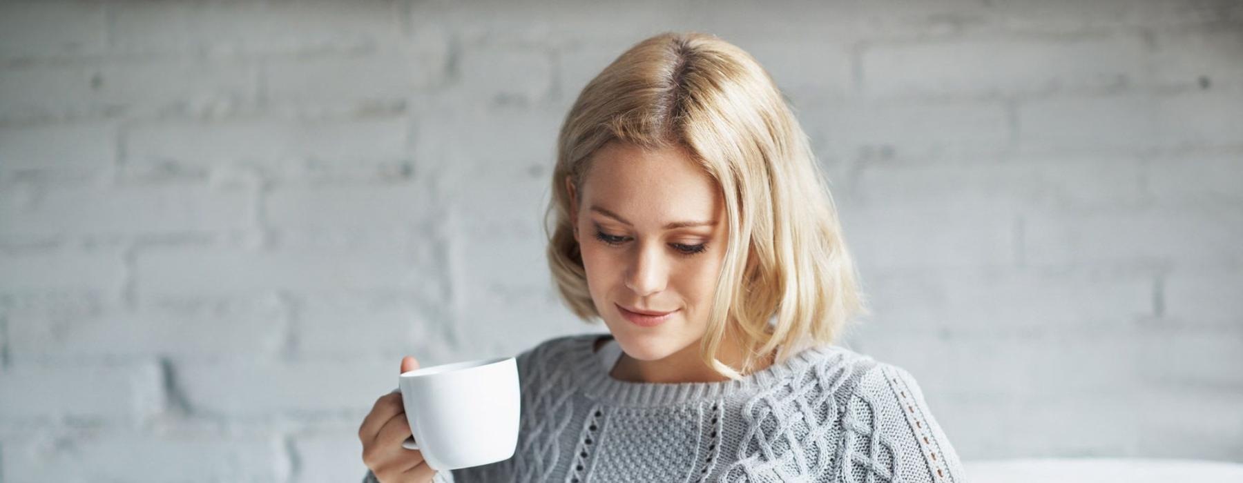 a woman sits on a couch with a cup of coffee and looks at her tablet